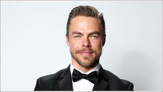 Derek Hough poses in a black suit against a white backdrop as Derek attends IMDb LIVE Presented By M&M'S At The Elton John AIDS Foundation Academy Awards Viewing Party on February 09, 2020 in Los Angeles, California.