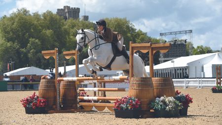Grey working hunter pony Ellas Melody jumps a fence at Windsor Horse Show with the castle visible in the background