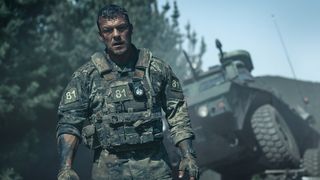 Alan Ritchson's US marine standing next to a ruined vehicle in Netflix's War Machine movie