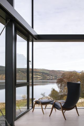 Black chair and footstool in living room overlooking lake and forest