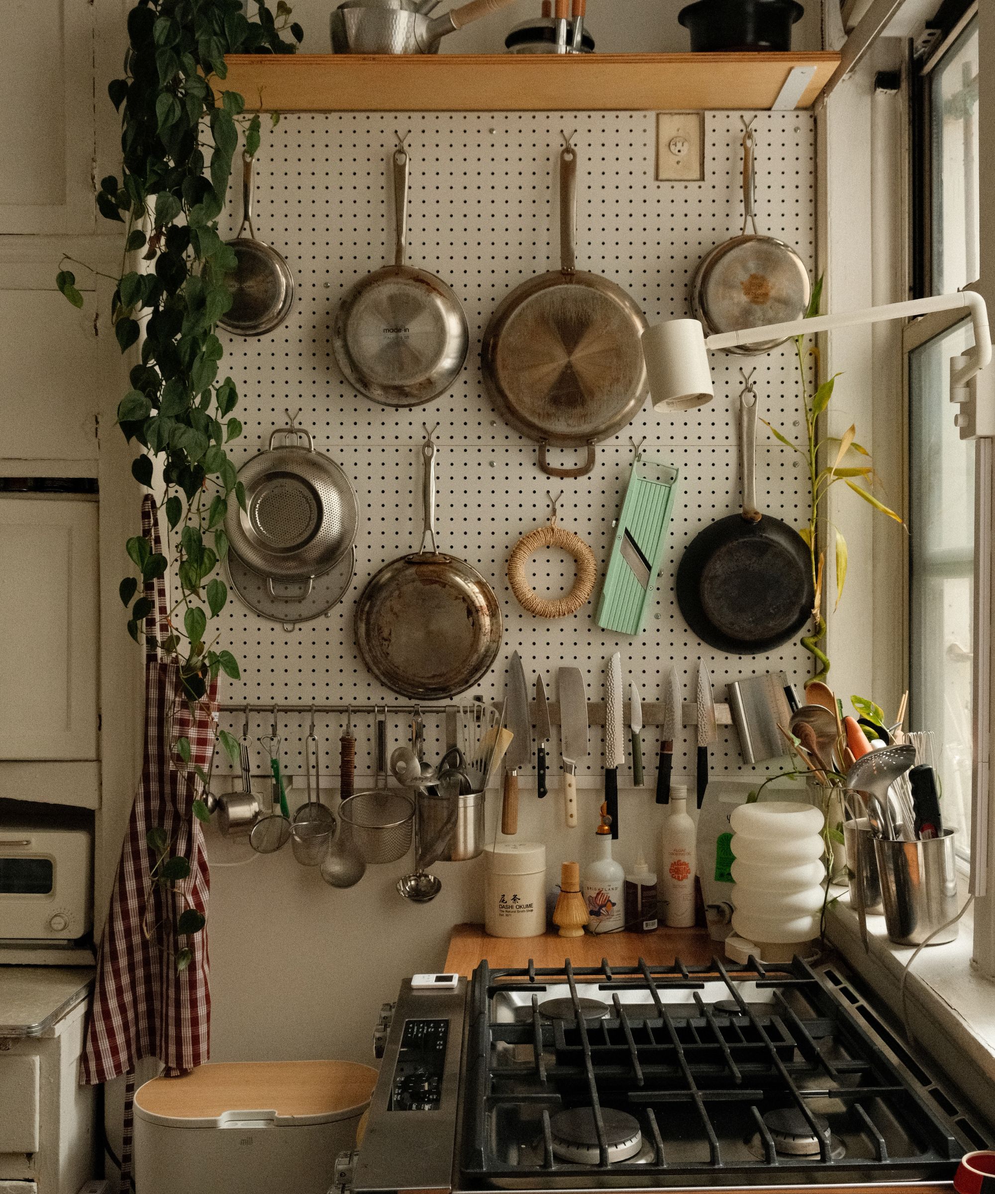 A small kitchen with a pegboard on the wall beside the cooktop to store additional pots and pans