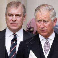 Prince Andrew wears a suit with a navy and red striped tie as he stands behind his brother King Charles, who is also wearing a suit