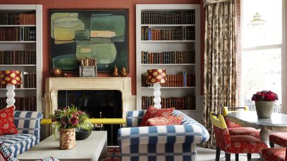 Fall color schemes in a living room with burnt orange walls, blue and white striped sofas and sand-colored mantel