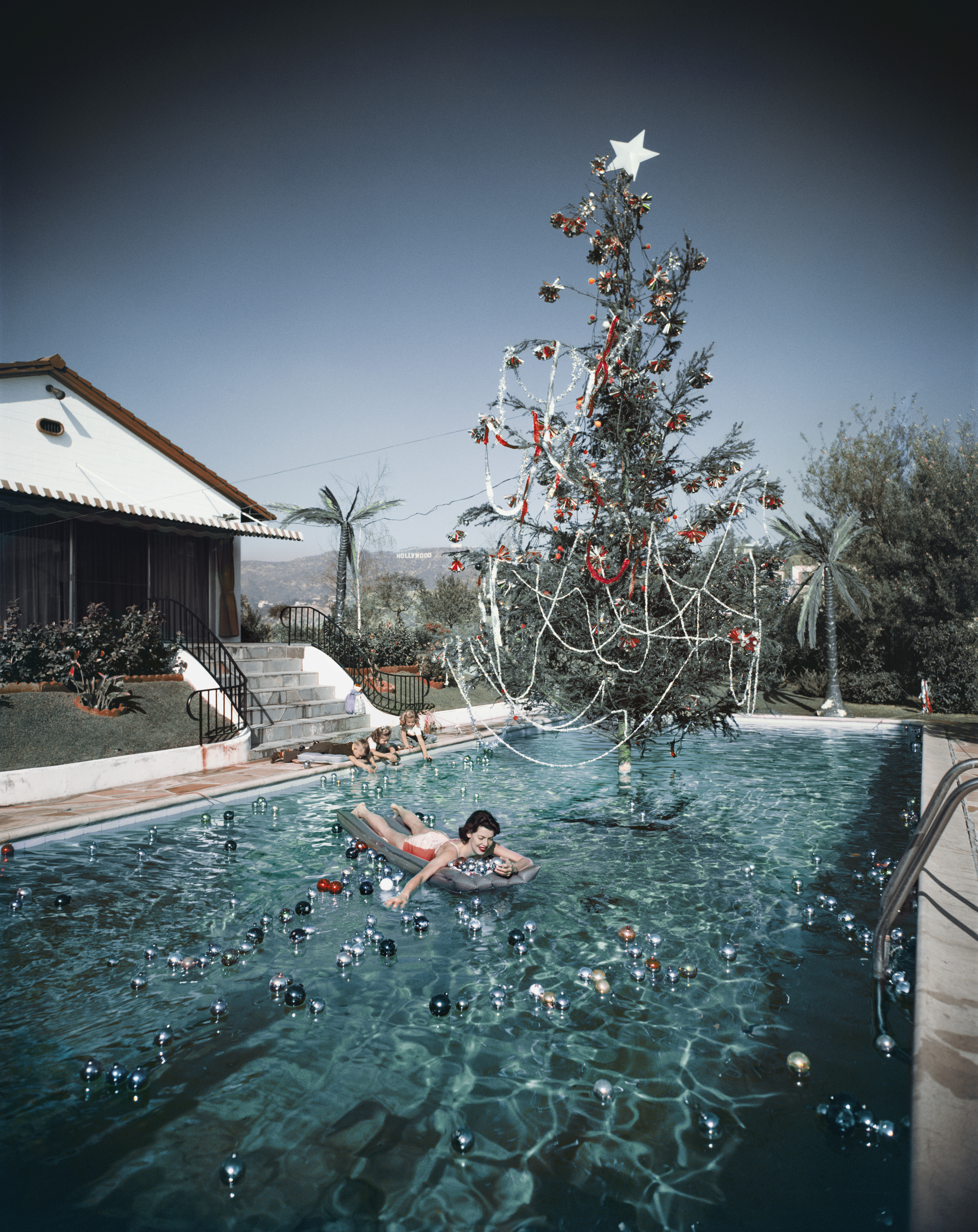 Rita Aarons, wife of photographer Slim Aarons, swimming in a pool festooned with floating baubles and a decorated Christmas tree
