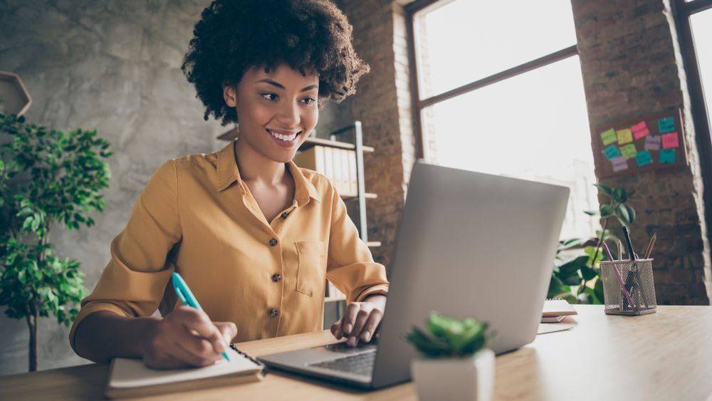 A woman smiling while sitting at a table and using a laptop