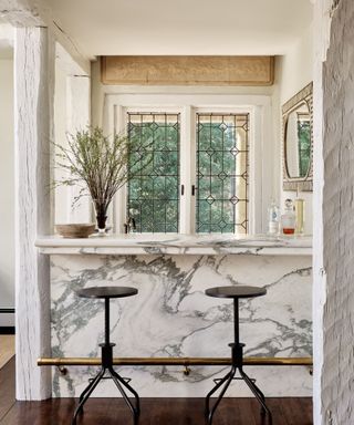 marble clad home bar with two stools and metal detail window behind