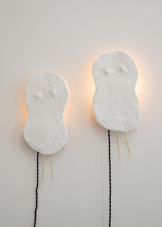 Pair of white bean-shaped plaster lamps with black cords and light visible behind