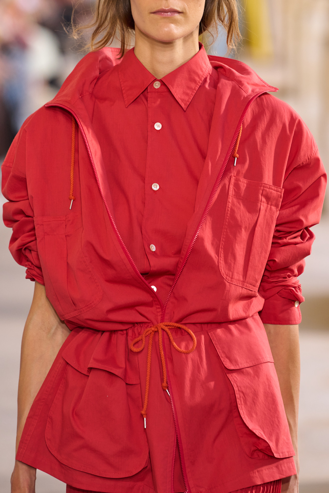 a woman wears a red sporty jacket over a red button-down shirt.