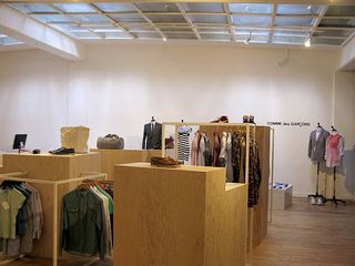 Tres Bien Shop, Sweden. A clothing store with clothing displayed on rails, mannequins and shelves with a wooden floor and a square skylight.