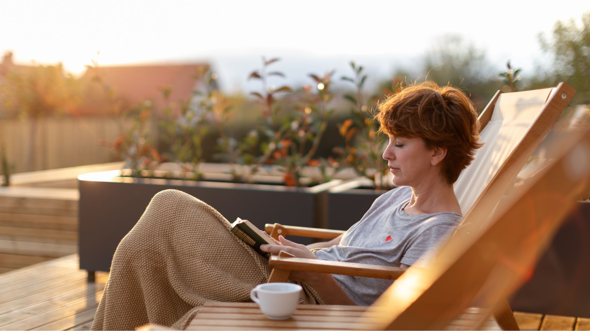 Woman drinking coffee and reading book sitting outside