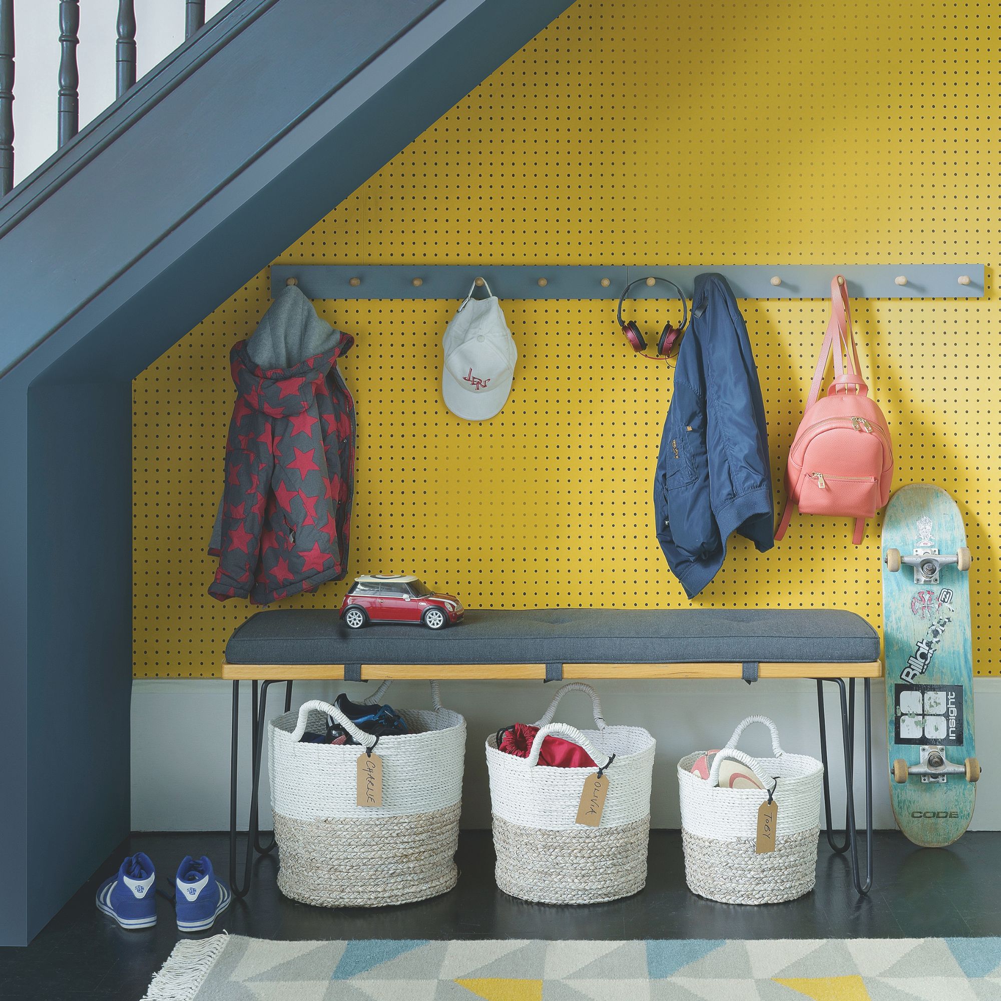 under the stairs storage area, with a bench, coat hooks on the wall, and storage baskets on the floor