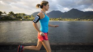Check out these Cyber Monday running headphones deals. Shown here, a woman running while wearing earbuds and a smartphone on her arm.