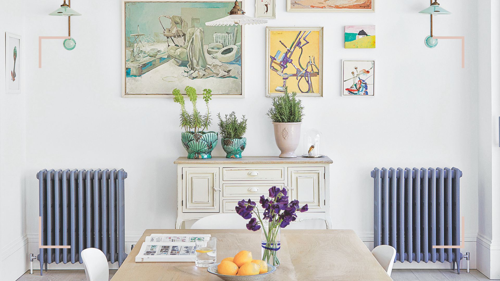 White dining room with a gallery wall and two blue radiators either side of a cream wooden sideboard
