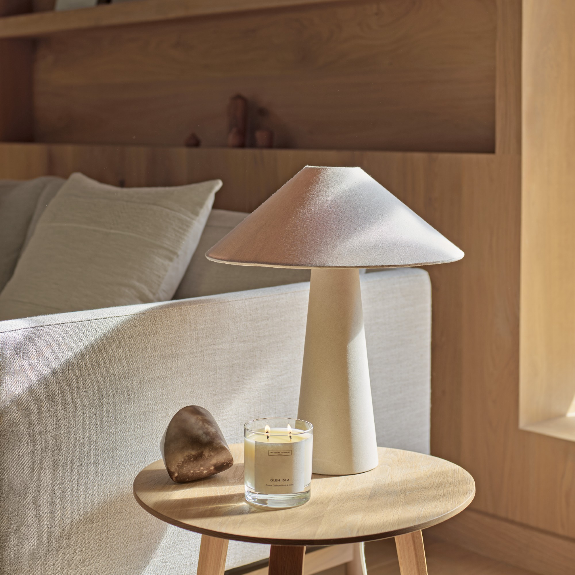 The White Company Glen Isla candle lit on a sofa side table next to a white table lamp