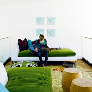 living room with white wall sofa with green cushion and lady with guitar