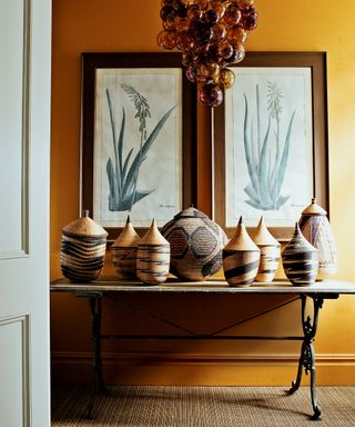An entryway with yellow wallpaper, botanical artwork and a collection of African baskets on a table.