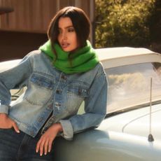 Woman wearing denim jacket and green scarf leaning on car