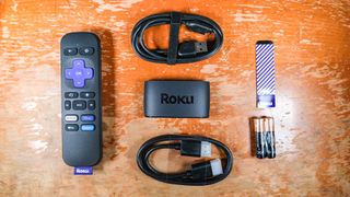 (clockwise) the parts inside the Roku Express (2022) are a USB cable, adhesive strip, two AAA batteries, an HDMI cord, the Roku Express itself and the Roku remote