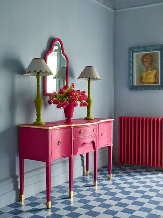 Pale blue room with blue and white checkered floor tiles, a pink painted radiator and desk