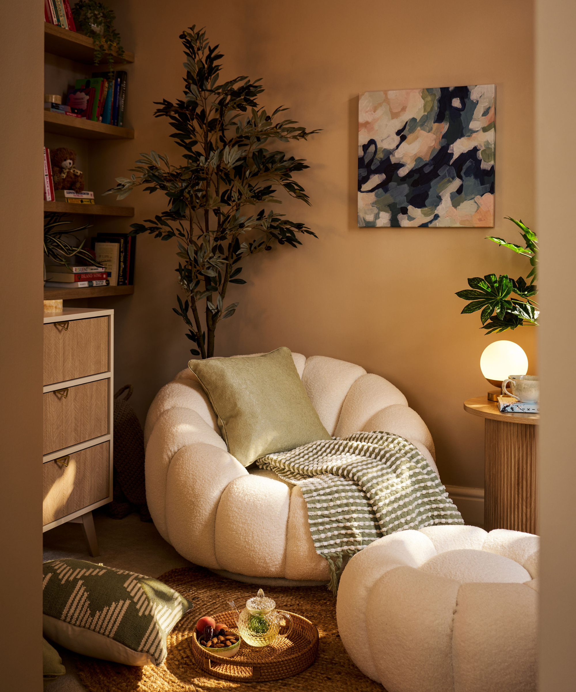Corner with white chair and matching foot rest, plant behind, and table with plant and light to the right