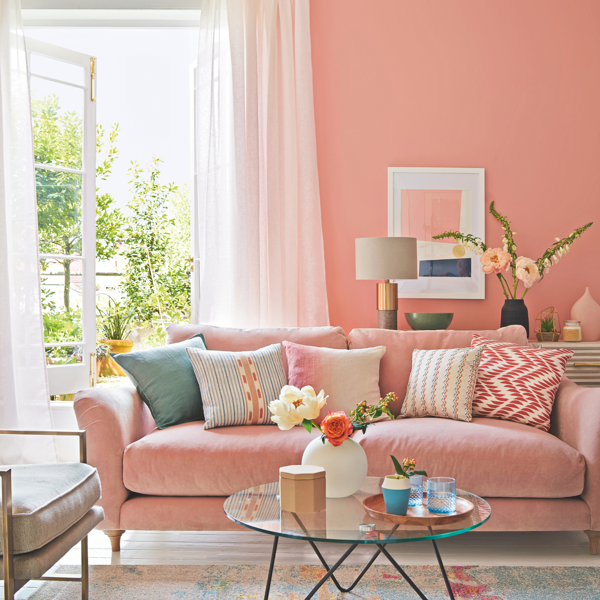 Living room with pink walls, white floor and curtains, French windows open to the garden, and furniture and decorations in pastel blues, pinks, and yellows
