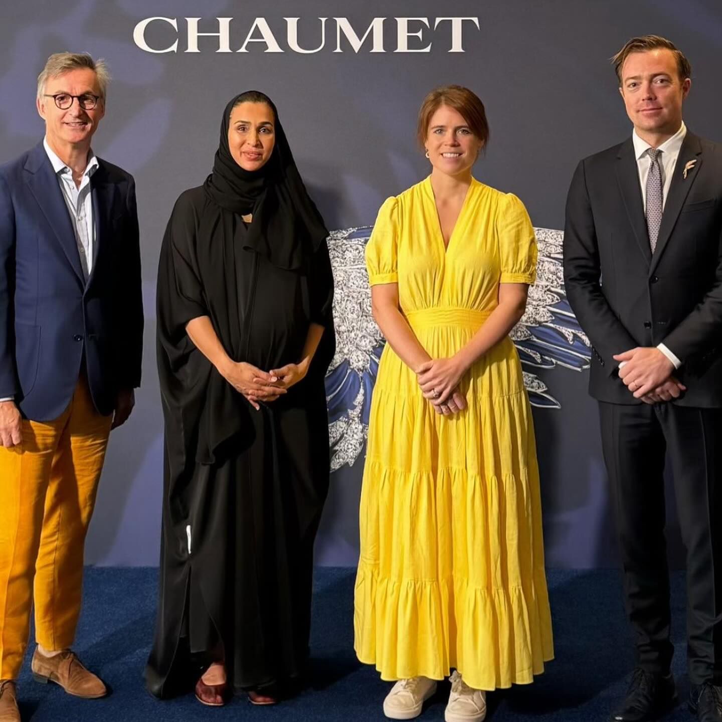 Princess Eugenie posing with two men in suits and a woman wearing a black head scarf in front of a backdrop reading