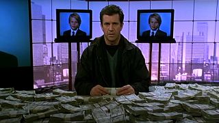 Mel Gibson sitting in front of a pile of ransom money on TV in Ransom.