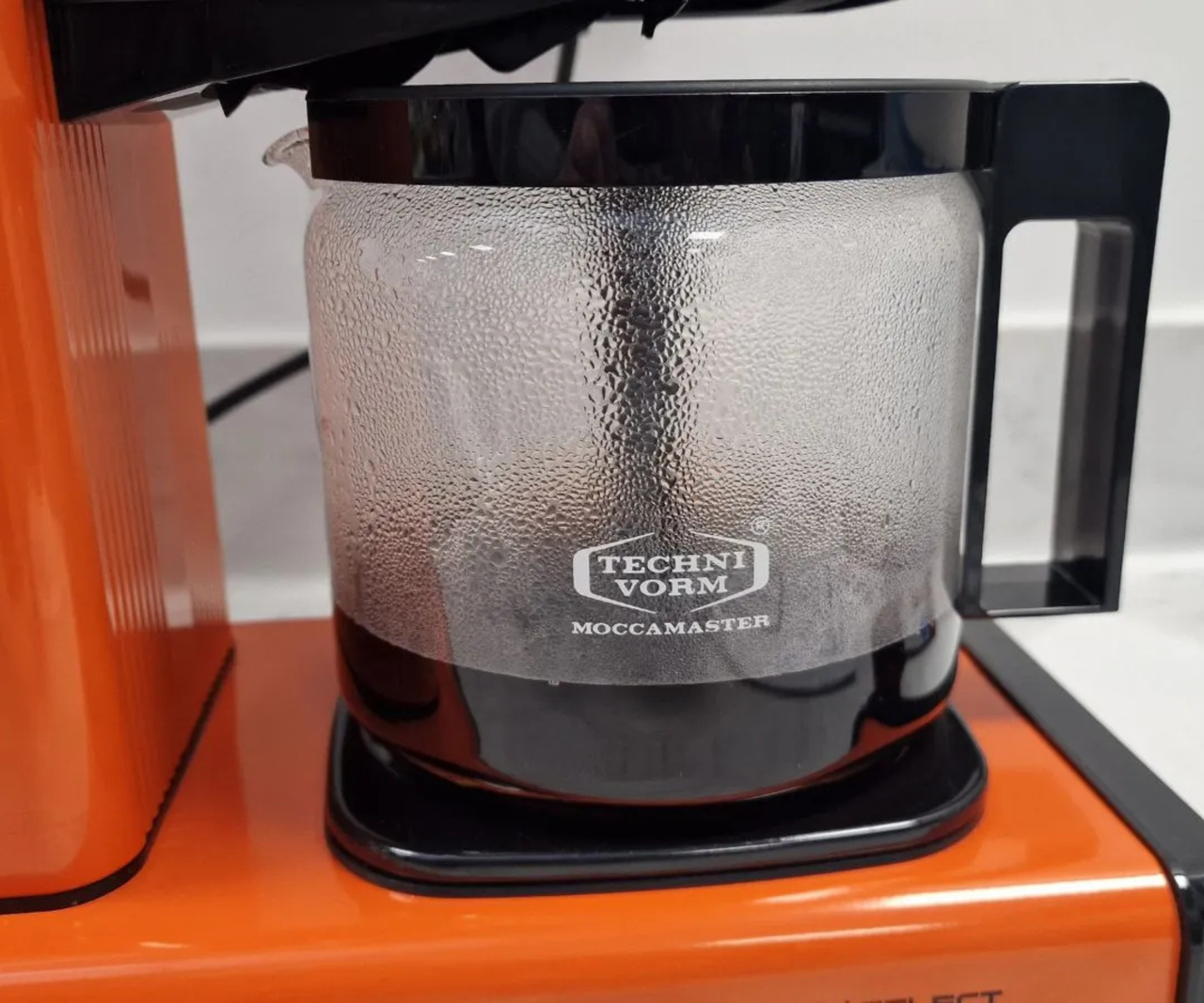 A bright orange Technivorm Moccamaster filling a stout glass carafe with coffee.