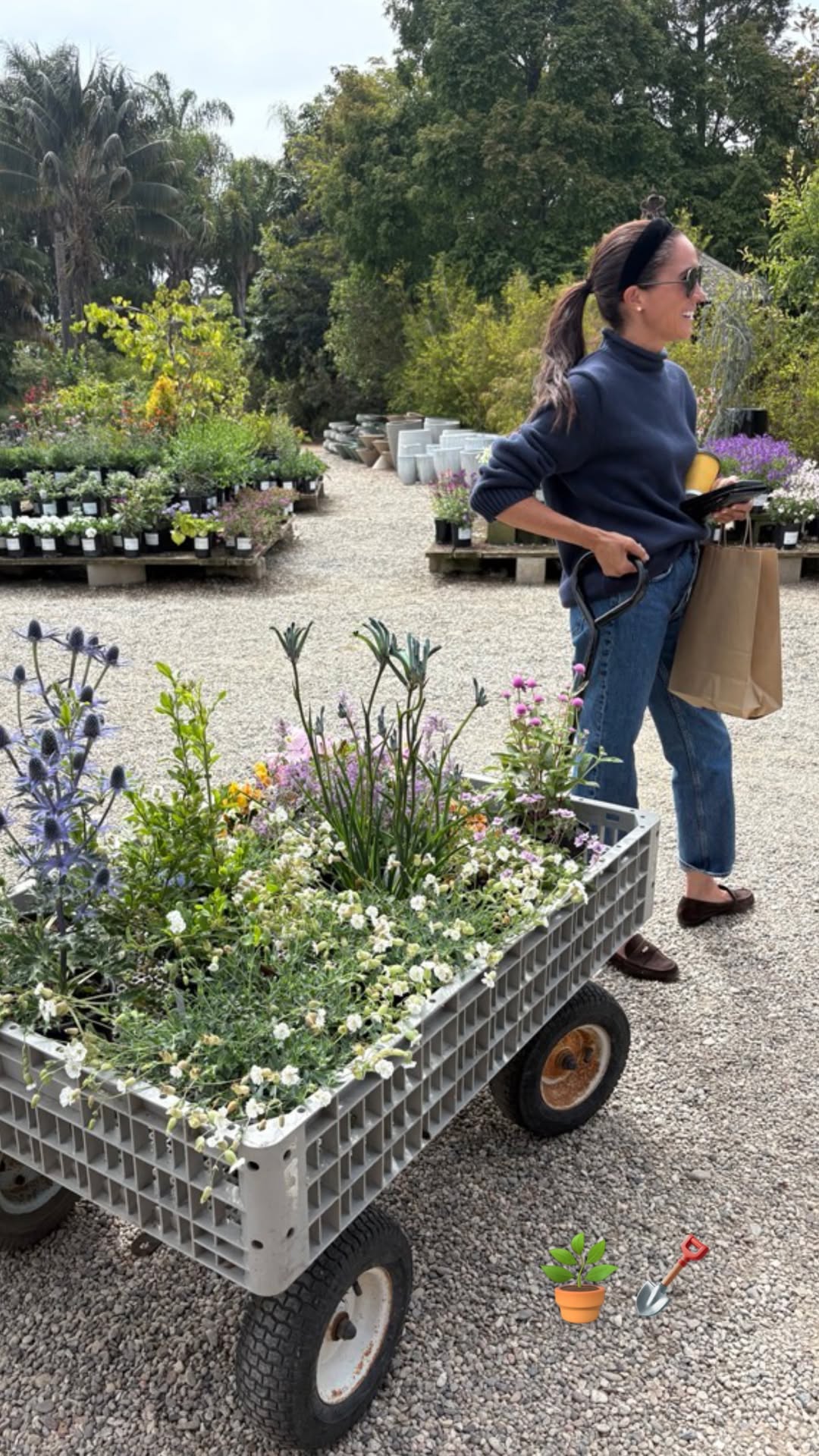Meghan Markle wears jeans, loafers, and a rollneck sweater and pulls a gray cart of flowers and shrubs