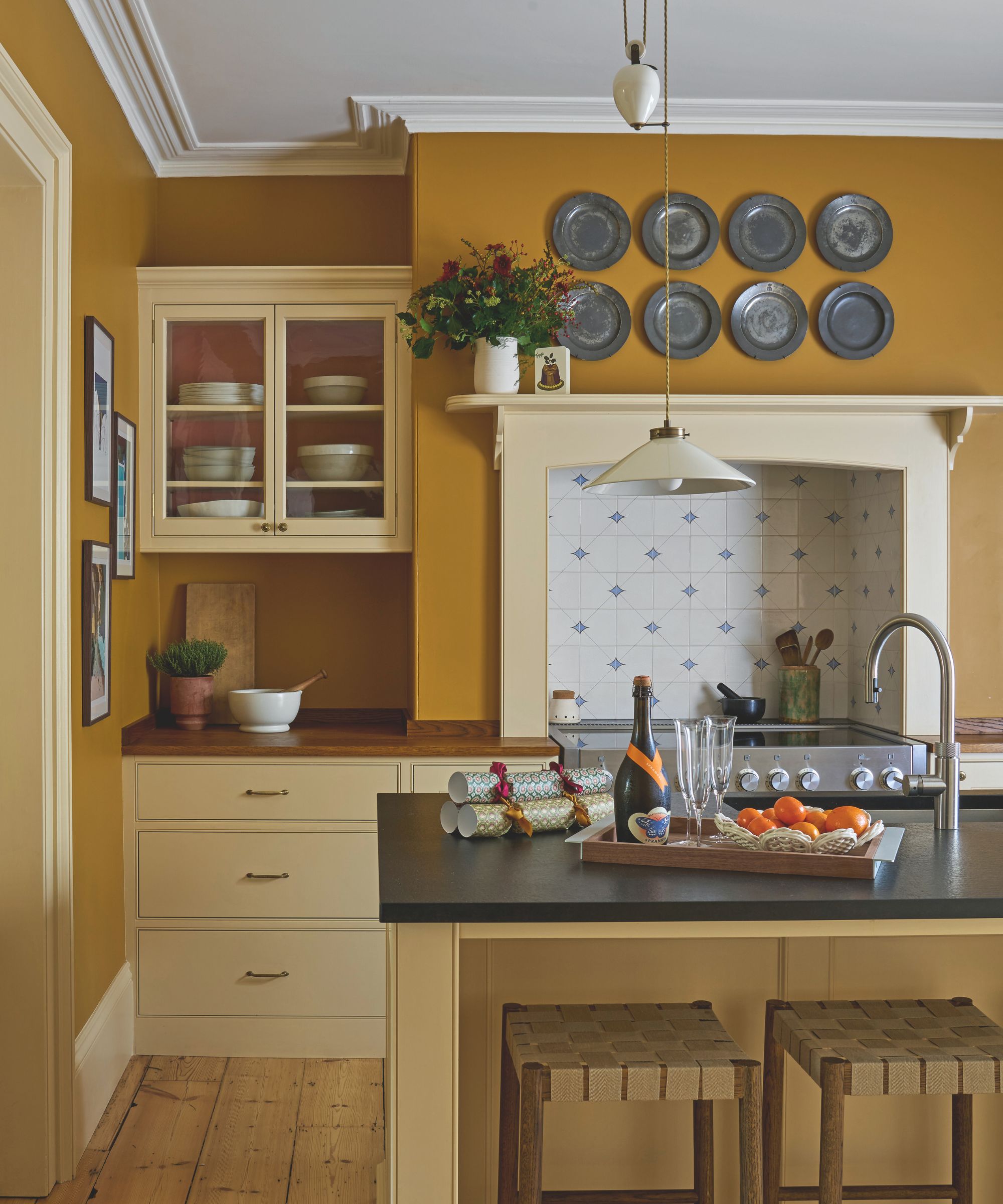 Yellow kitchen with dark yellow walls and lighter cabinetry. There is an island in the middle and a range with delft tiles