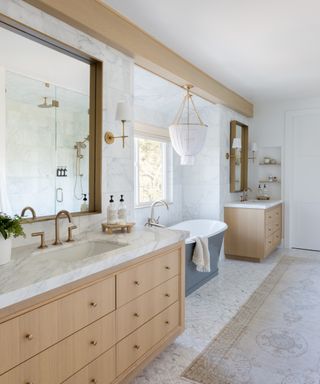 bathroom with twin wood-effect vanity units with blue freestanding bathtub between and marble topped cabinets