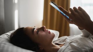 woman lying on her bed on her phone looking upset