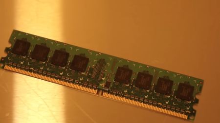 A green computer RAM module with multiple black chips is placed on a reflective gold surface, under warm lighting, creating a tech-focused atmosphere.