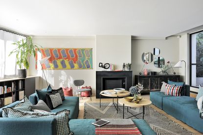 Living room with wood floor, teal L shaped sofa, occasional tables and modern art