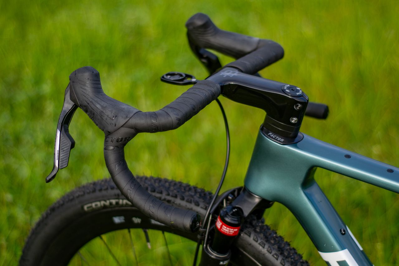 A blue Factor Sarana gravel bike in a grassy field with a hedge in the background