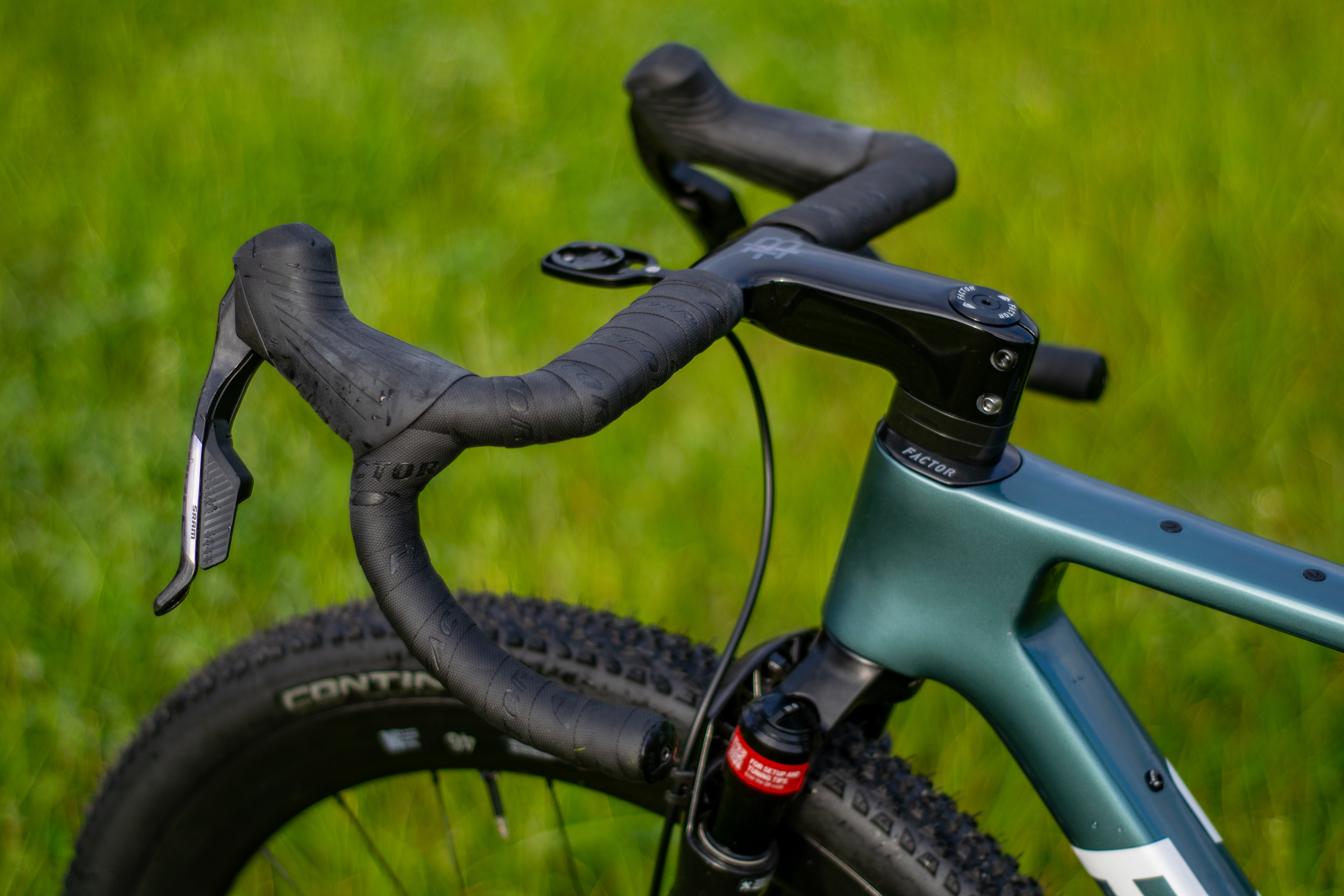 A blue Factor Sarana gravel bike in a grassy field with a hedge in the background