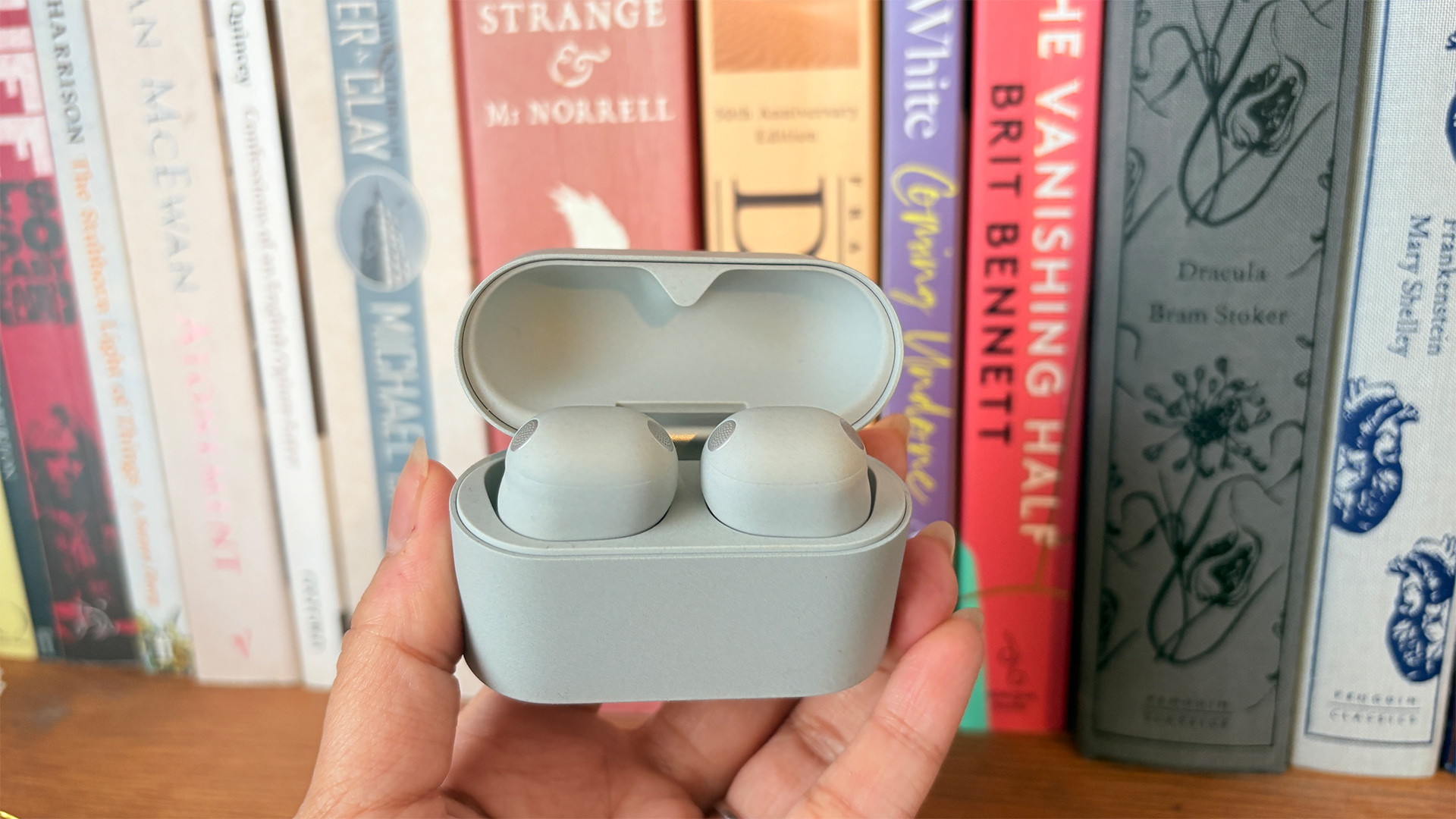 Sony WF-1000XM6 wireless earbuds in case held in hand in front of books