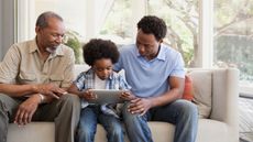 Black grandfather, son, and grandson sitting on a coach looking at a book