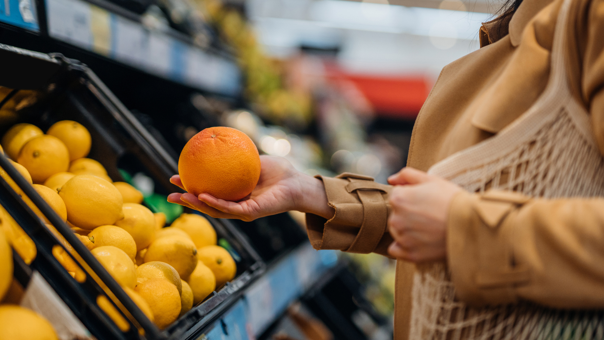 a woman picks up an orange at the grocery store