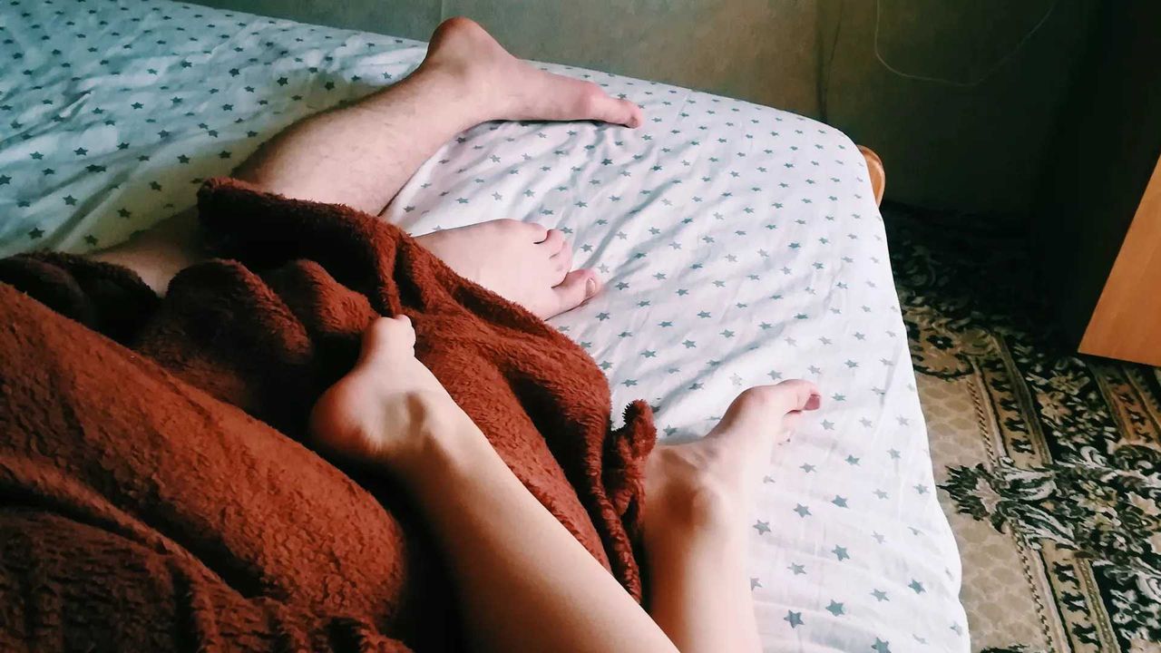 couple&#039;s legs and feet in bed with red blanket over them