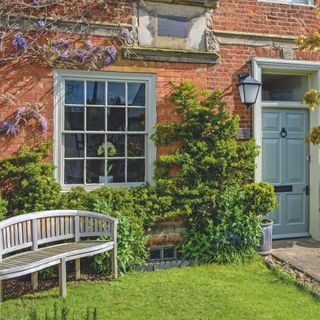 Exterior of a sash window and front door of a period home, with climbing plants on the wall and a bench in front of the window