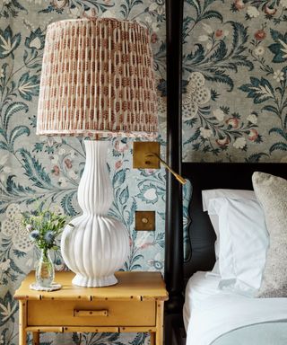 A bedroom with a white sculptural lamp on a side table and bright patterned wallpaper on the walls
