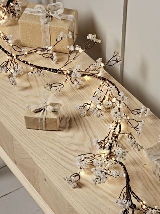 faux branch with fairy lights on a wooden table, gold wrapped presents