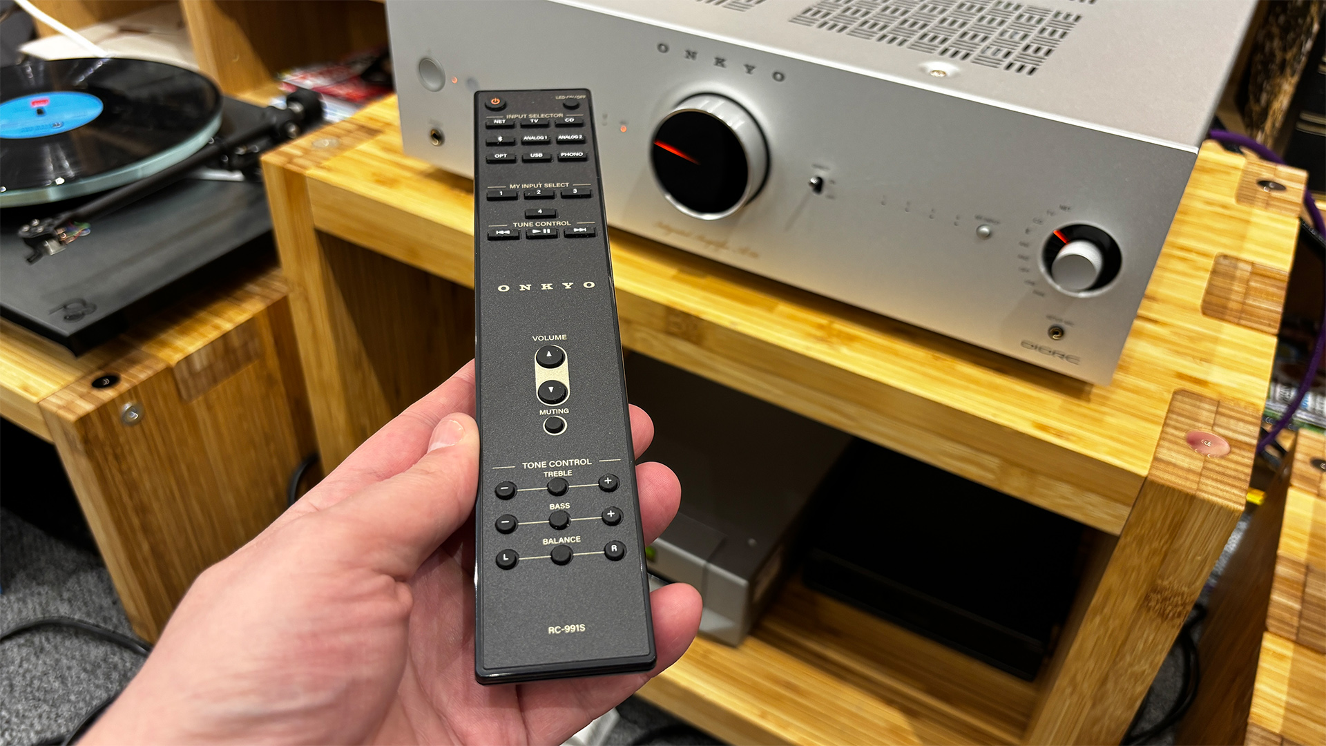 Onkyo Icon A-50 streaming amplifier on wooden hi-fi rack with remote control held in hand above it