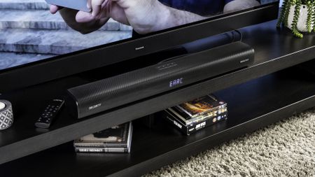 majority elias, a black soundbar with a silver majority logo, and a hdmi earc port and optical port, with a black remote, photographed on a black TV stand