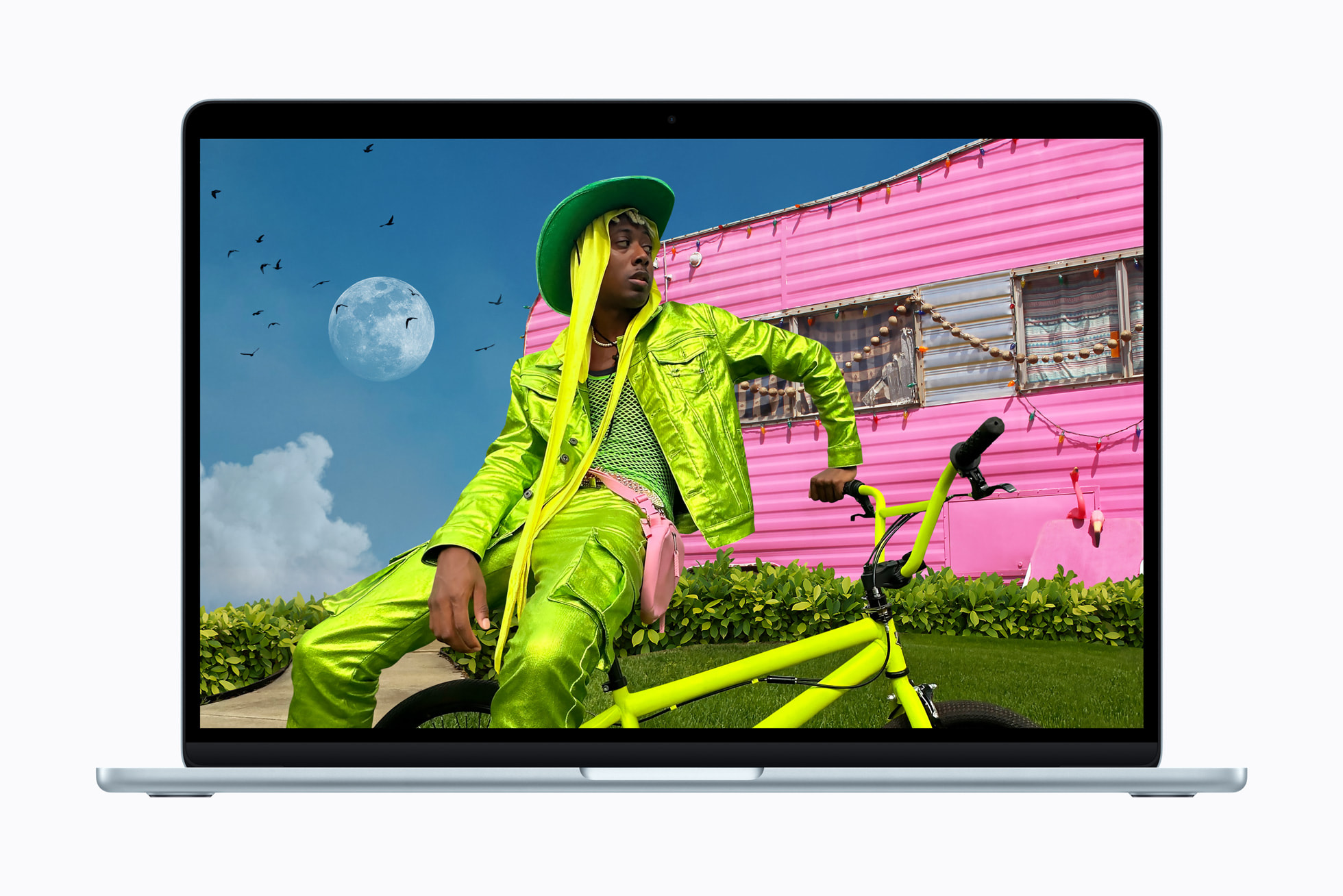 A MacBook Air screen showcases a high-saturation photo of a person in reflective lime-green clothing posing on a yellow bicycle in front of a bright pink building.