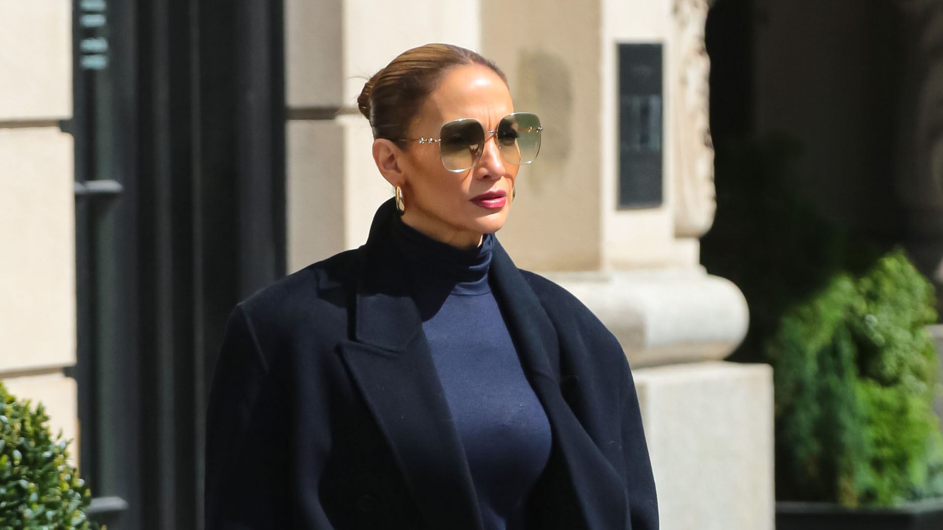 Jennifer Lopez wearing black coat, black turtleneck, blue jeans, blue boots, and sunglasses