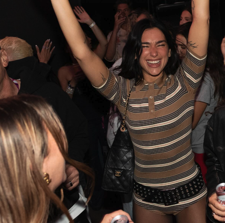 Dua Lipa wearing a striped Prada matching set and carrying her Chanel 25 bag