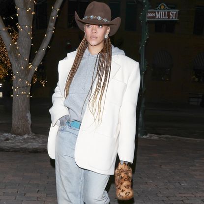 Rihanna wearing a western hat with a grey hoodie, a white blazer, and baggy jeans