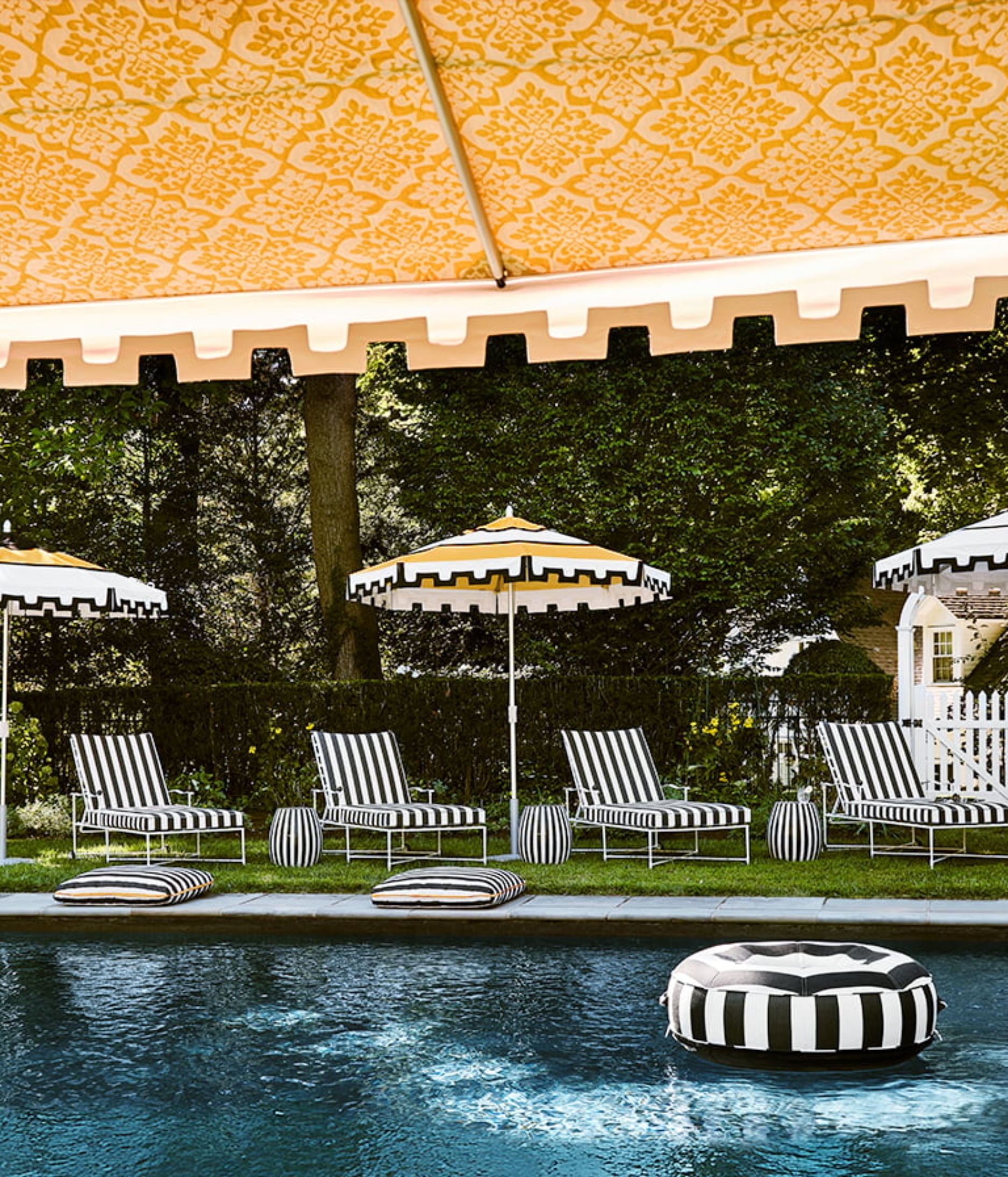a pool side with black and white striped outdoor loungers and a yellow black and white parasol.